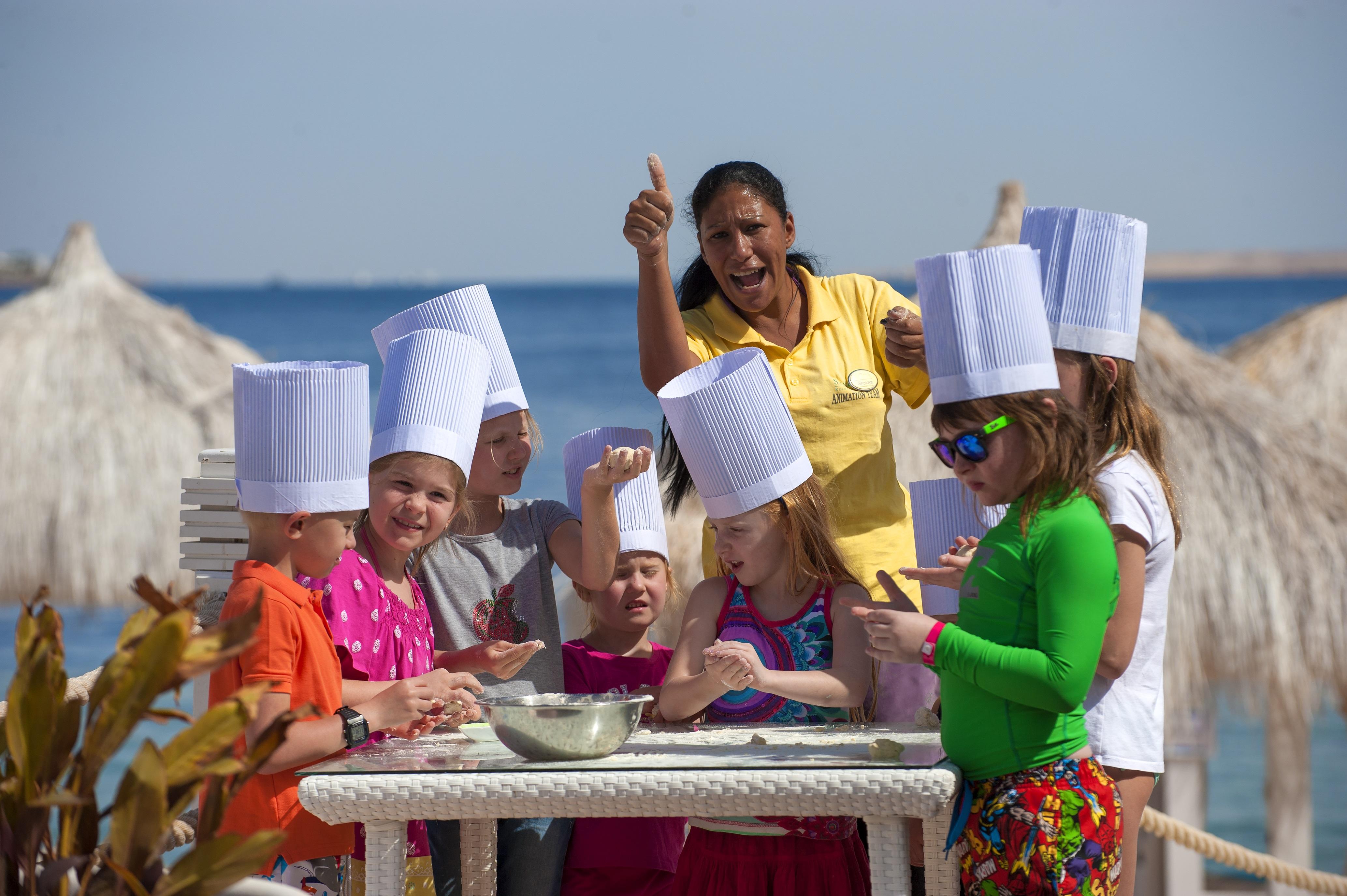 Sunrise Arabian Beach Resort Sharm el-Sheikh Exteriör bild The photo shows a group of children, all wearing white chef hats, gathered around a table. They appear to be engaged in a cooking activity, possibly making something together. A woman, likely a instructor or leader, is standing among them, giving a t